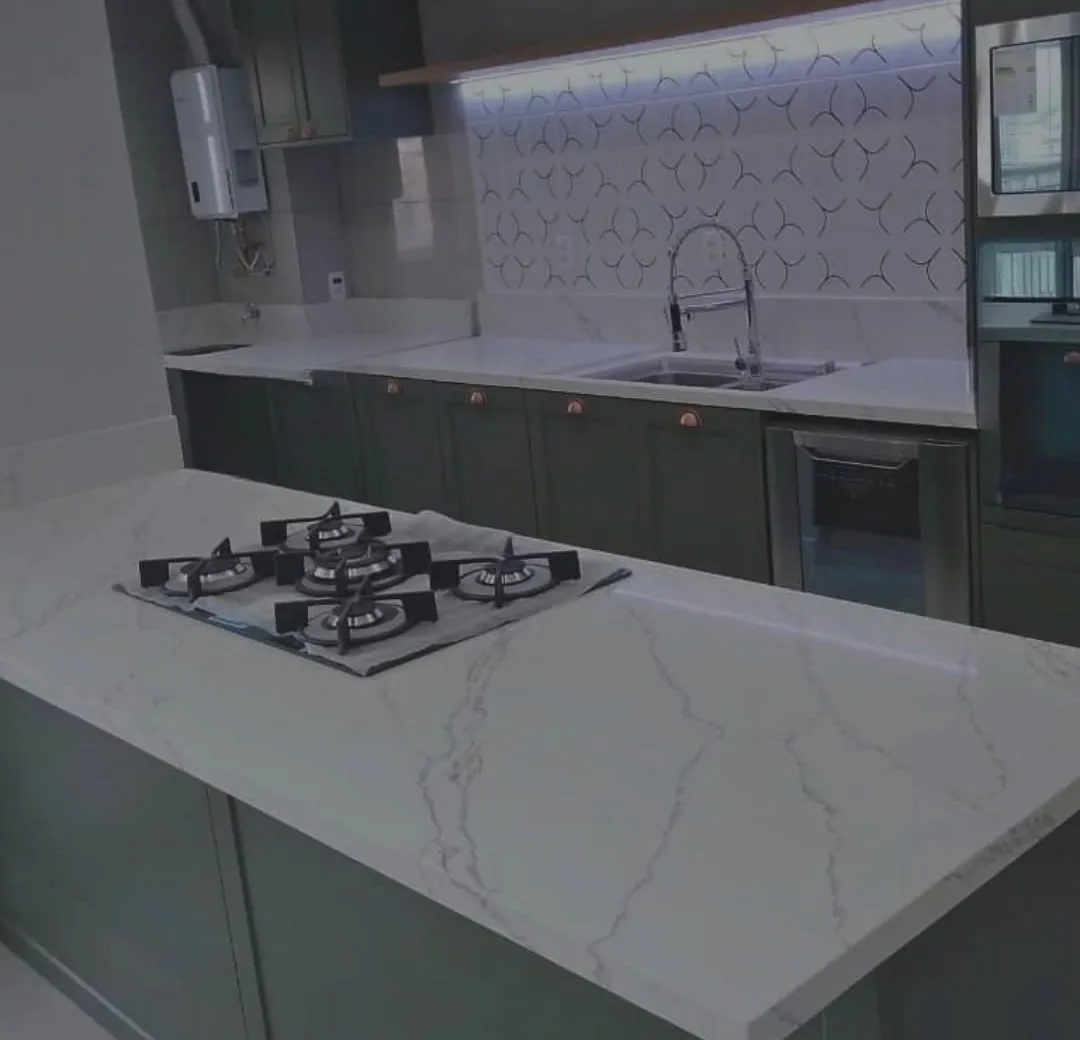 Cozinha com ilha em pedra branca de veio cinza, cooktop embutido e armários verdes